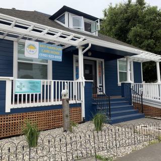 A blue house with a white porch and several business signs, featuring landscaping and decorative fencing.