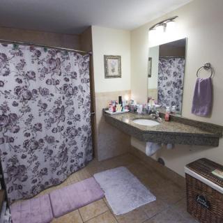 A cozy bathroom featuring a floral shower curtain, a countertop with toiletries, and pastel-colored bath mats and towels.