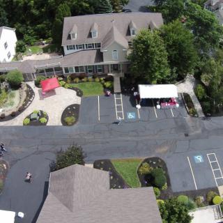 Aerial view of a house surrounded by trees with a parking lot and driveway.