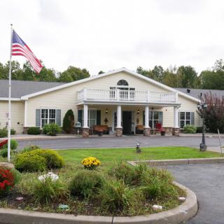A well-maintained nursing home building with an American flag and landscaped gardens at the entrance.