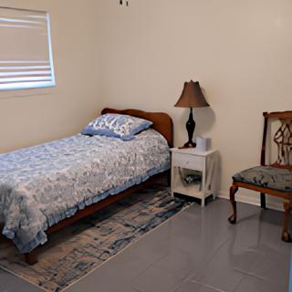 A minimalist bedroom featuring a single bed, nightstand with a lamp, and a chair.