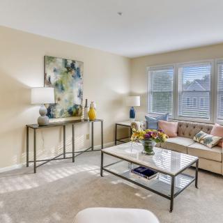 A bright and welcoming living room with modern decor, featuring a comfortable sofa, coffee table, artwork, and large windows.