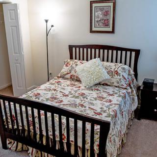 A cozy bedroom featuring a wooden bed frame with floral bedding and a standing lamp.