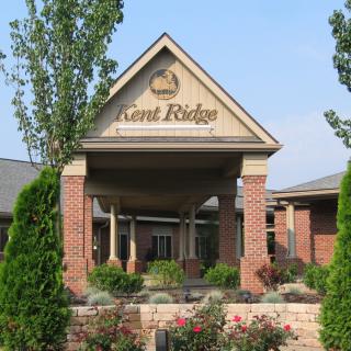 The image shows the entrance of a building with a sign reading 'Mard Ridge'. It features brick pillars, a triangular roof, and manicured landscaping.