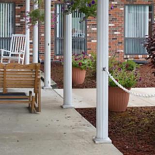 A cozy porch with a swing, rocking chair, and decorative columns next to a brick building.