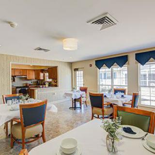 A well-lit dining area with neatly arranged tables and chairs, adjacent to a kitchen space.