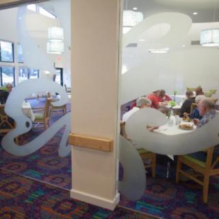 A cozy restaurant interior with people dining at tables, featuring patterned carpets and frosted glass decor.