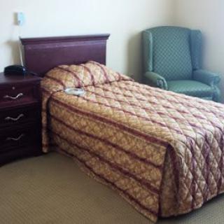 A neatly arranged bedroom with a single bed, upholstered headboard, nightstand, and armchair.
