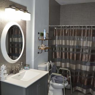 A modern bathroom with a vanity, oval mirror, and striped shower curtain. Safety equipment is installed near the toilet.