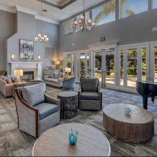 A spacious and elegantly designed living room featuring comfortable seating, a grand piano, and large windows that allow natural light to flood the space.