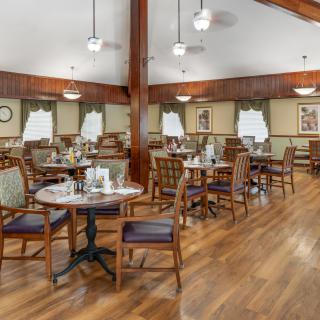 A cozy dining room with neatly arranged tables and chairs, featuring wood flooring and warm lighting.
