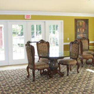 An elegant dining area with ornate chairs and a round table, set on a patterned carpet in front of large windows.