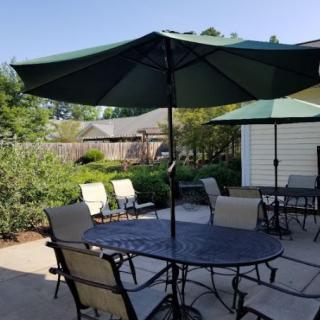 A sunny patio with outdoor furniture and umbrellas in a backyard setting.
