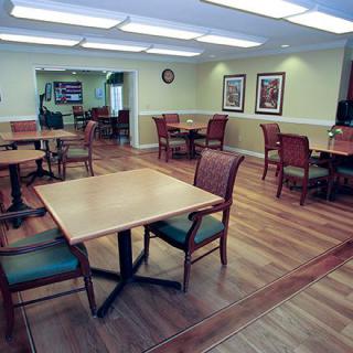 An empty dining room with wooden tables and chairs, featuring paintings on the walls and bright lighting.