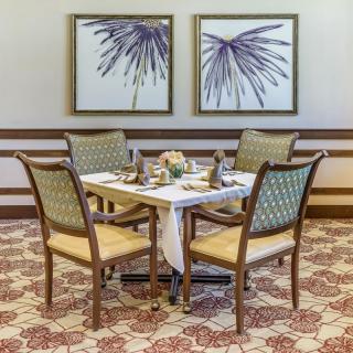 An elegantly set dining table with four chairs, complemented by artwork on the wall and patterned carpeting.