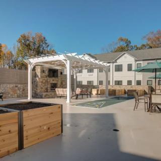 A modern outdoor patio area featuring a pergola, seating, and landscaped surroundings on a sunny day.