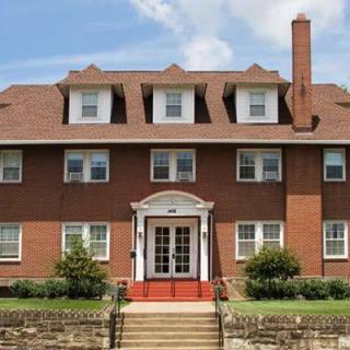 Front view of a large brick residential house with a prominent entrance and multiple dormer windows.
