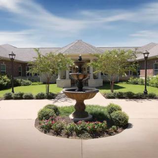 A beautiful courtyard with a central fountain surrounded by lush greenery and a pathway leading to a building.