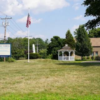 A grassy area featuring an American flag, a gazebo, and a building under a partly cloudy sky.
