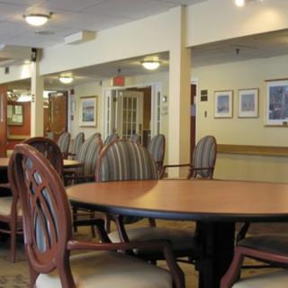 A neatly arranged dining area with wooden tables and chairs, featuring soft lighting and decorative wall art.