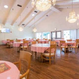 A spacious dining area with pink tablecloth-covered tables, wooden chairs, and elegant chandeliers.