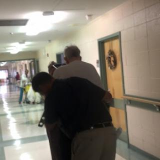 A candid moment captured in a hallway where two individuals are sharing an interaction.