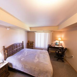 A cozy bedroom with a large bed, wooden furniture, and a work desk by the window.