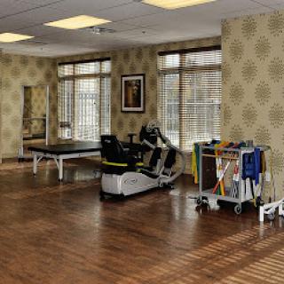 A well-lit rehabilitation gym featuring various fitness equipment and a warm wooden floor.