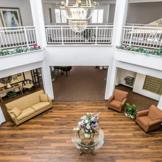 A spacious lobby area with wooden flooring, featuring a central decorative table and comfortable seating arrangements under an elegant chandelier.