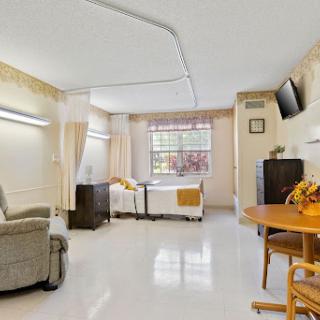 A well-lit hospital room featuring a bed, comfortable chair, and a dining table, designed for patient care.