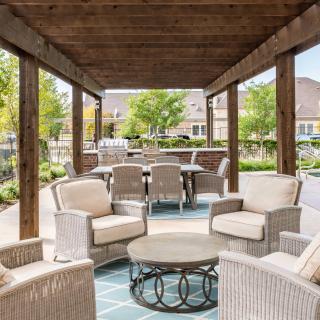 An inviting outdoor seating area under a pergola, featuring wicker chairs and a coffee table with a garden view.