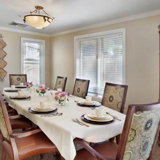 A well-decorated dining room featuring a long table set for a meal with elegant chairs and floral centerpieces.