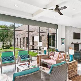 A modern living room with ample natural light, featuring stylish furniture and large windows that overlook a green outdoor space.