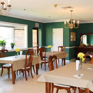 A neatly arranged dining room with wooden furniture and green walls, adorned with floral centerpieces.
