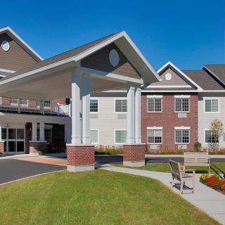 A modern senior living facility with a landscaped entrance and clear blue skies.