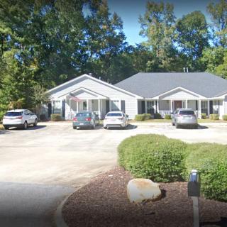 A residential building with a driveway and parked cars surrounded by trees and bushes.