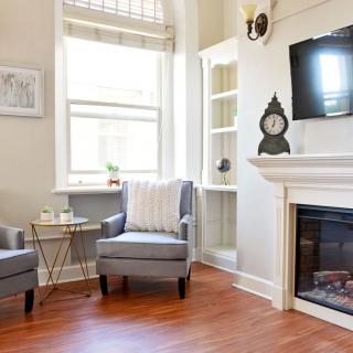 A cozy living room with a fireplace, two gray chairs, and a mounted television.