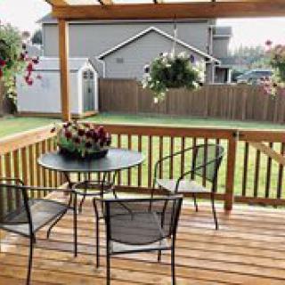 A cozy backyard patio with a wooden deck, complete with a table and chairs surrounded by colorful flowers and hanging plants.