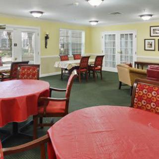A cozy dining area with multiple tables covered in red tablecloths, arranged in a well-lit community space.