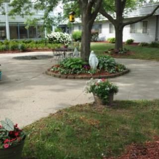 A tranquil garden courtyard with a central tree surrounded by flowers and greenery.
