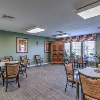 A cozy dining area with multiple tables and chairs, featuring warm lighting and large windows.