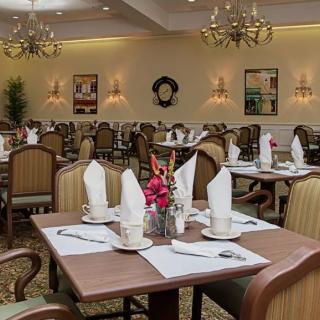 Elegant dining room setup with neatly arranged tables and chairs, featuring decorative chandeliers and classic table settings.
