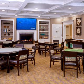 A well-furnished dining room featuring multiple tables and chairs, a fireplace, bookshelves, and a wall-mounted television.