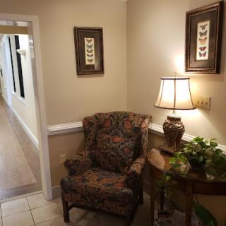 A cozy waiting area featuring a floral patterned chair, decorative lamp, and wall art.