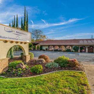 A welcoming entrance to a well-maintained property, featuring lush landscaping and a clear blue sky.