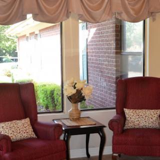 A cozy corner of a living room featuring two red chairs and a small table with a flower arrangement.