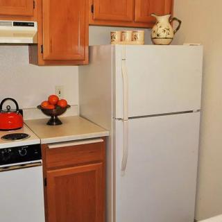 A compact kitchen space featuring a white refrigerator, wooden cabinets, and a countertop with a fruit bowl and teapot.