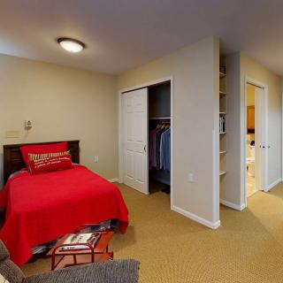 A cozy bedroom with red bedding and an open closet, featuring a carpeted floor.