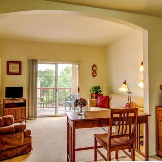 A cozy living room with a desk, comfortable seating, and natural light from the balcony door.