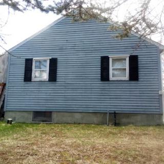 A simple blue-sided house with black shutters and a grassy yard.